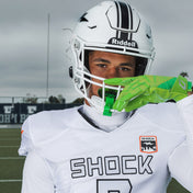 Football player in white Shock Doctor uniform and helmet wearing a chrome slime green Shock Doctor Max AirFlow Lip Guard on the field.