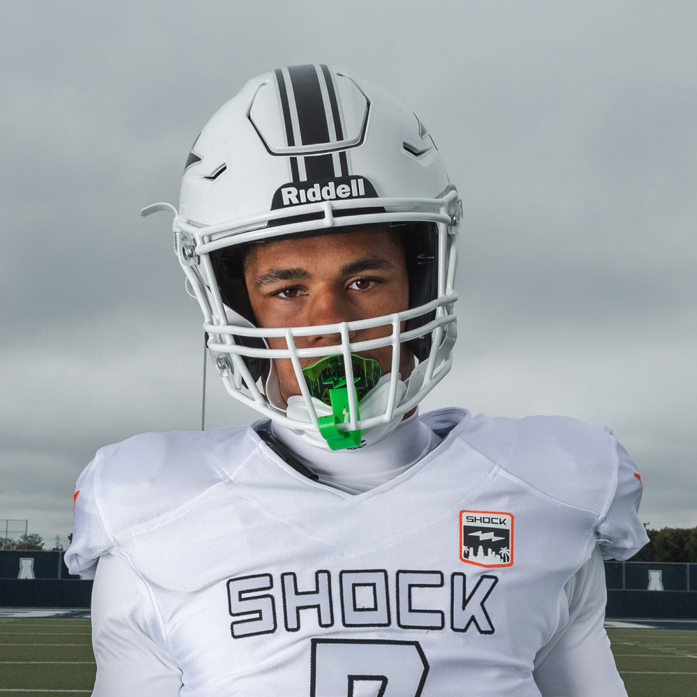Football player in white Shock Doctor uniform and helmet wearing a chrome slime green Shock Doctor Max AirFlow Lip Guard on the field