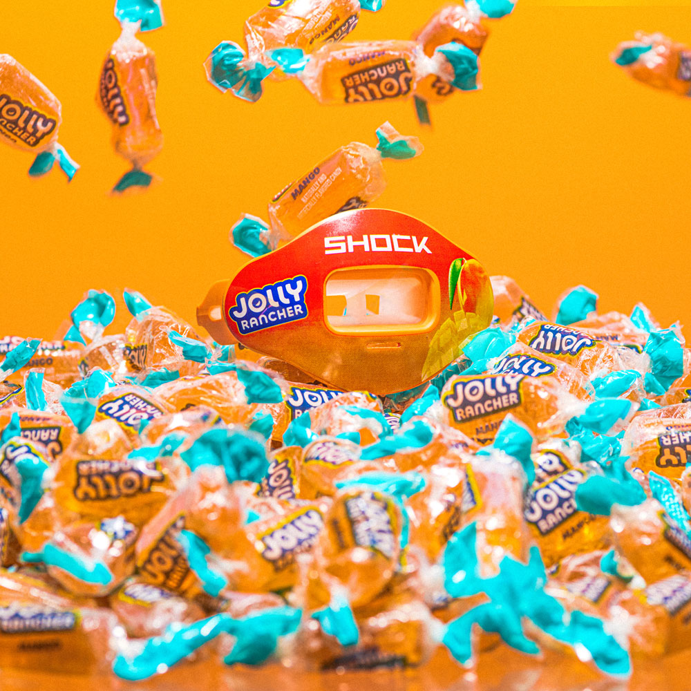 Lifestyle Shot of Shock Doctor Jolly Rancher Max AirFlow Football Mouthguard (Mango Flavor) Sitting on Bed of Jolly Ranchers