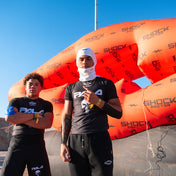 Two 7v7 football athletes standing in front of a large inflatable with 'Shock Doctor' branding. Wearing Shock Doctor White "Sheisty" Ski Mask
