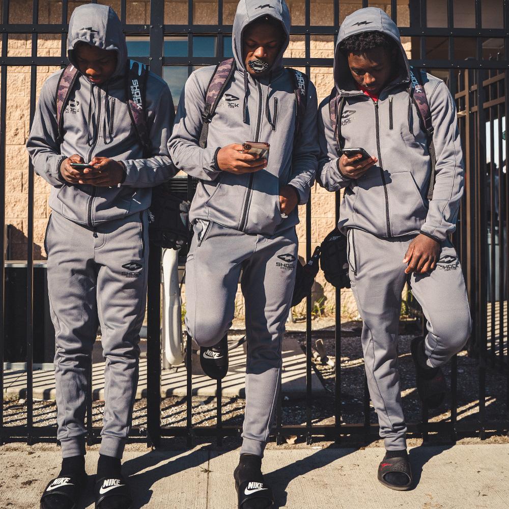 3 Youth Football Players Leaning Against a Fence Wearing Shock Doctor Athletic Zip-Up Hoodie in Grey