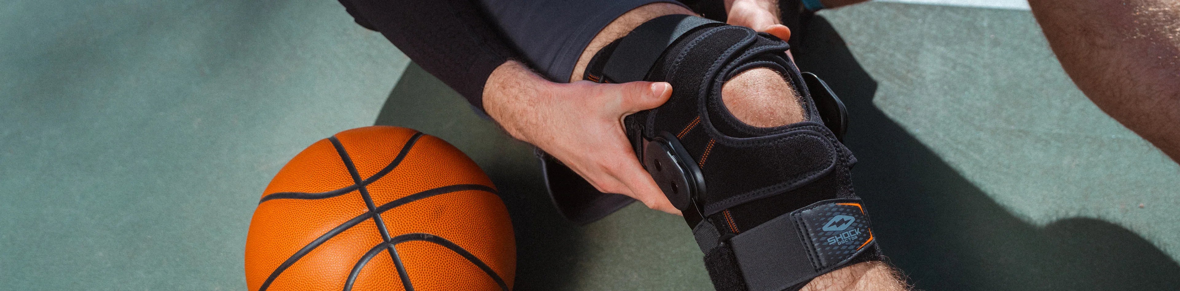 Basketball player adjusting a Shock Doctor knee brace next to a basketball on the court