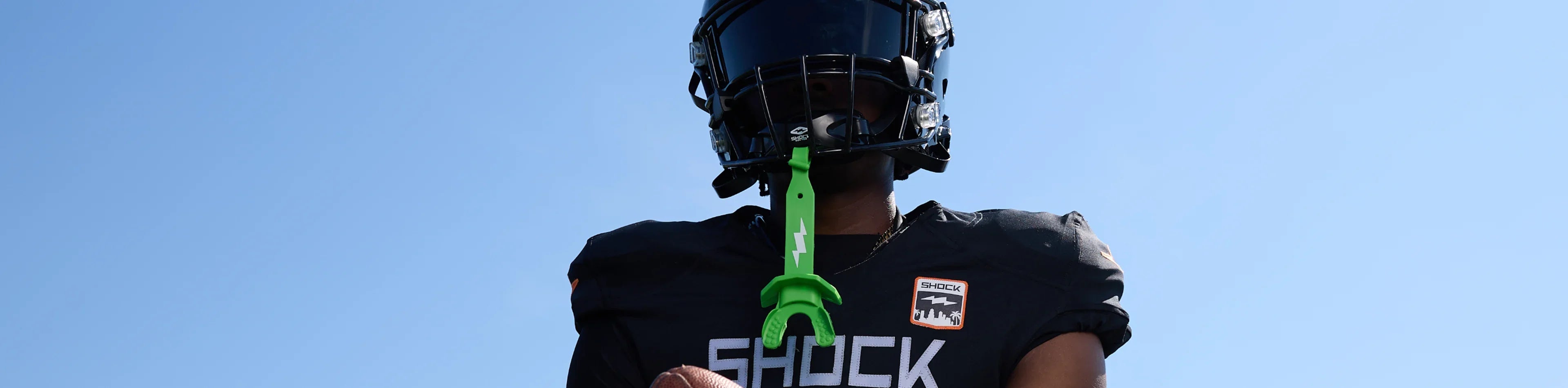 Football player wearing a green Shock Doctor thunderbolt lip guard against a blue sky