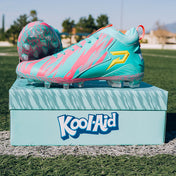 Kool-Aid Sharkleberry Fin cleats by Phenom Elite displayed on a teal Kool-Aid shoebox on a turf field