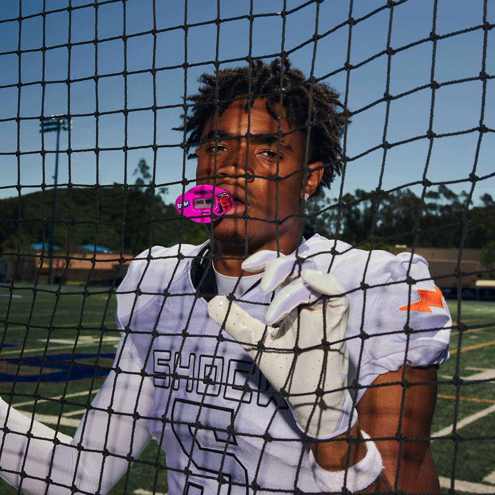 Youth athlete wearing Shock Doctor Kool-Aid Flavor Pink Lemonade Max AirFlow behind a net on a sports field