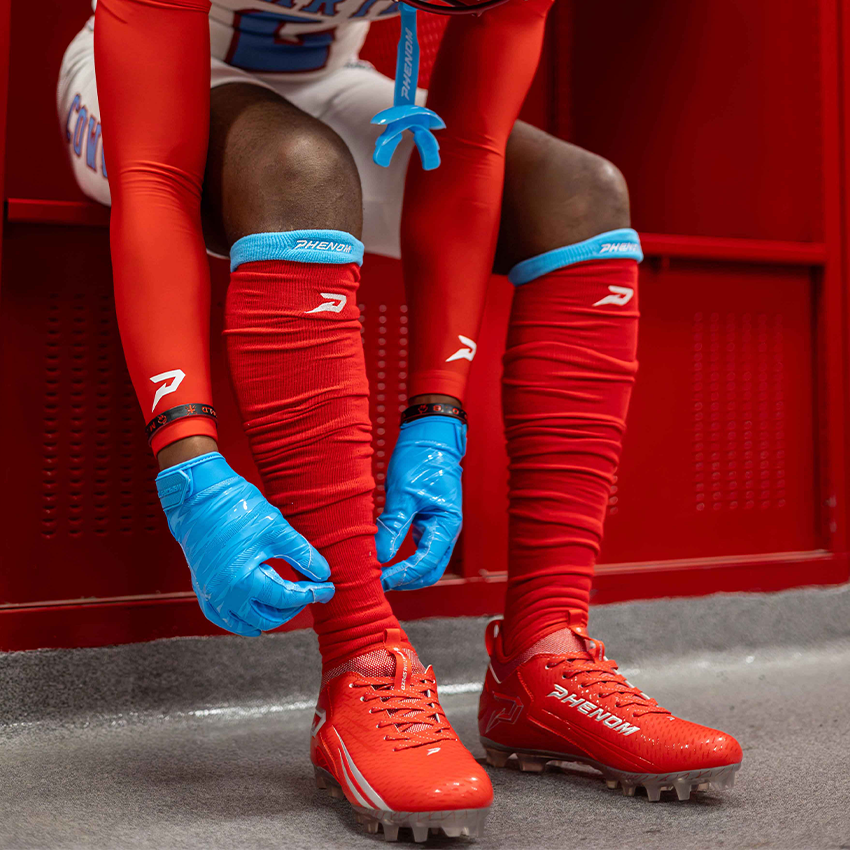 Tackle football athlete wearing red sports gear with blue football gloves sitting on a red bench.