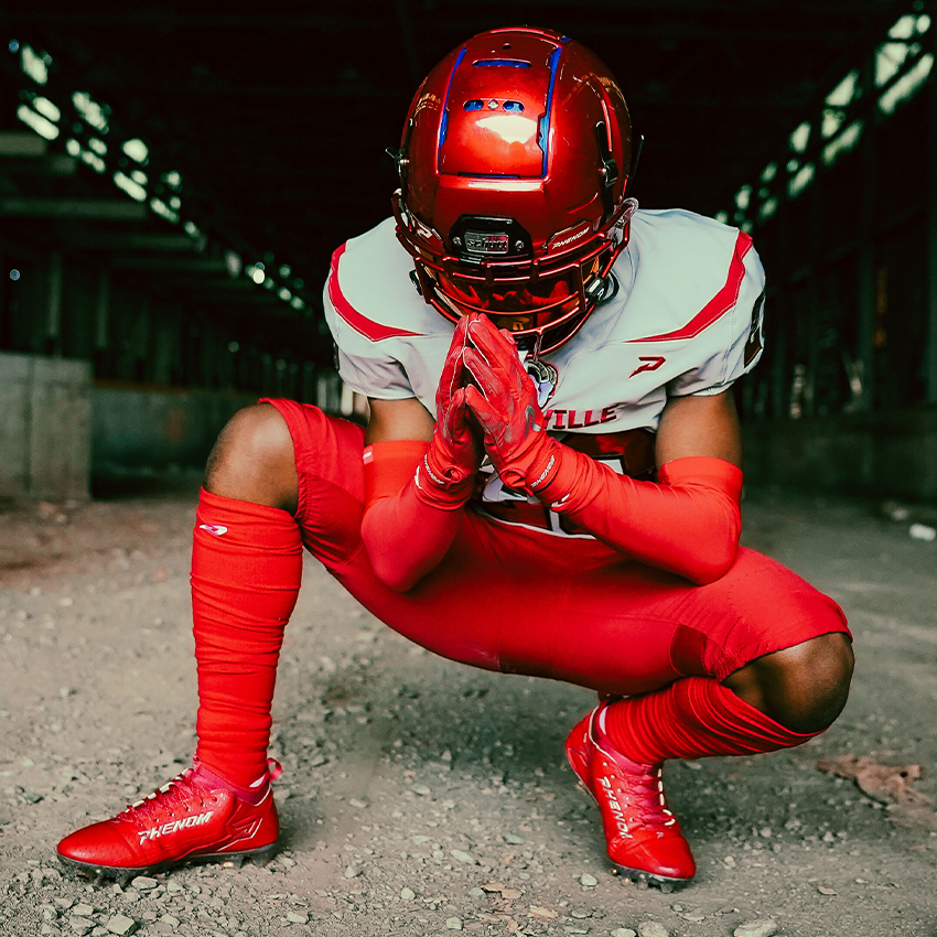 Tackle Football athlete in red and white football uniform kneeling on a dark road.