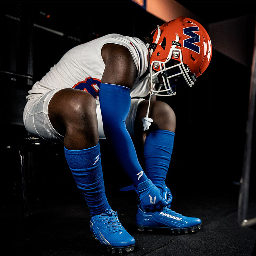 Football player in white uniform with blue socks and cleats, wearing an orange helmet with a logo.