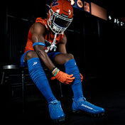 Football player in orange and blue uniform sitting on a bench.