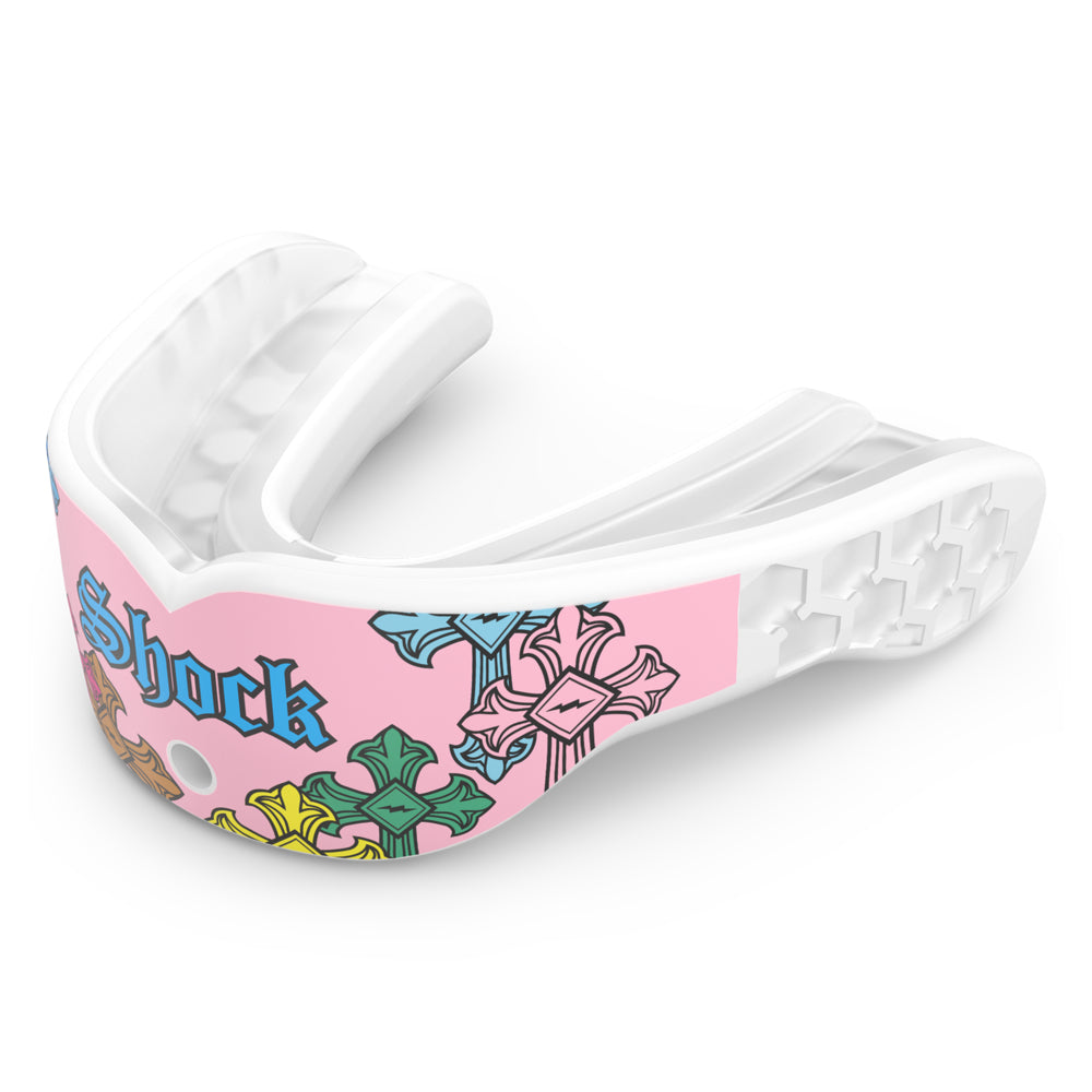 Shock Doctor Gel Max Power Print mouthguard in Pink Divine Drip, shown at a three-quarter angle. Pink and white mouthguard with multicolored gothic cross graphics in blue, green, yellow, and orange, "Shock" lettering in blue Old English script, and a honeycomb-pattern back channel with a center breathing hole.
