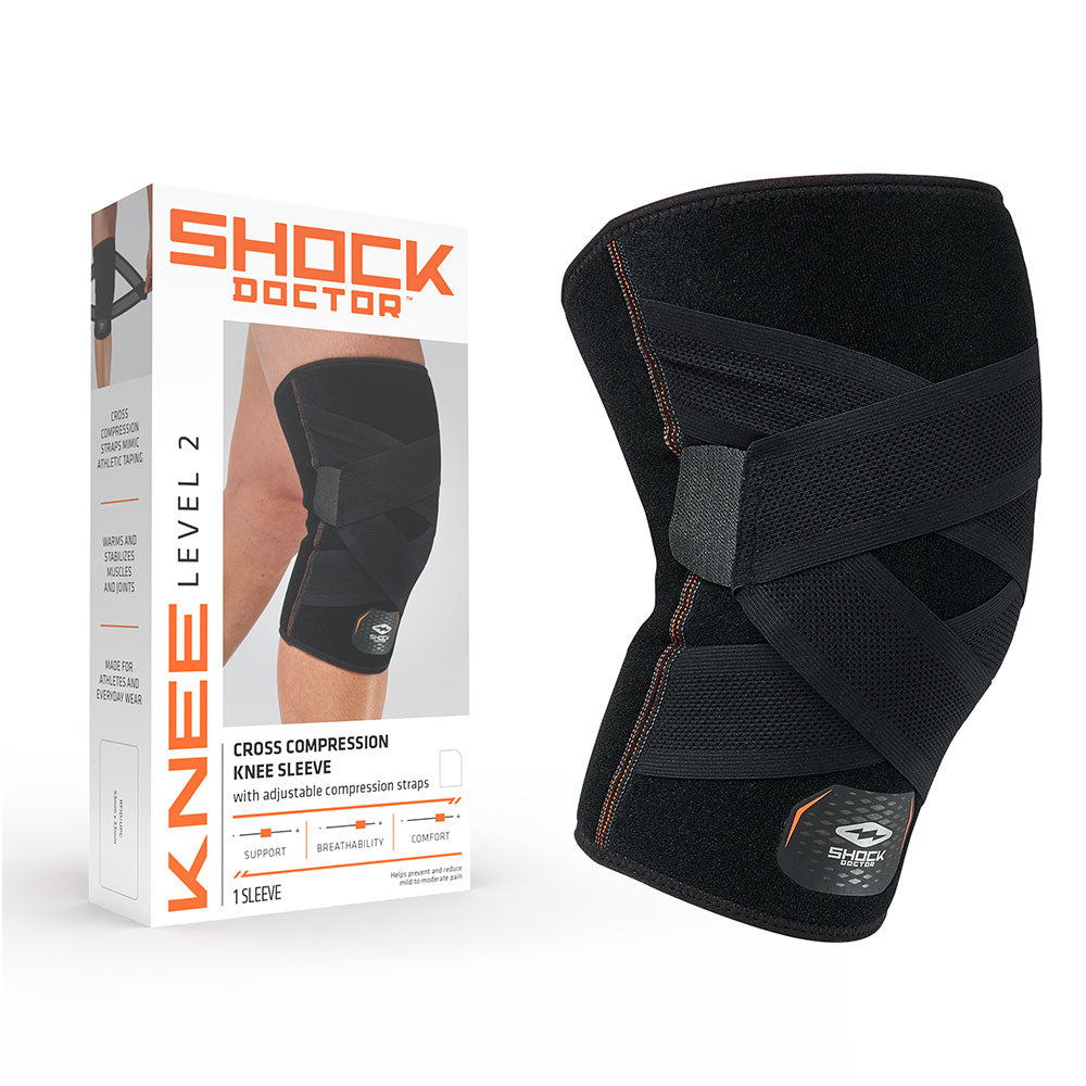 Shock Doctor Level 2 Cross Compression Knee Sleeve package next to product, black knee sleeve with crossing compression straps and adjustable hook-and-loop closures