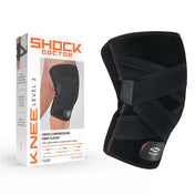Shock Doctor Level 2 Cross Compression Knee Sleeve package next to product, black knee sleeve with crossing compression straps and adjustable hook-and-loop closures