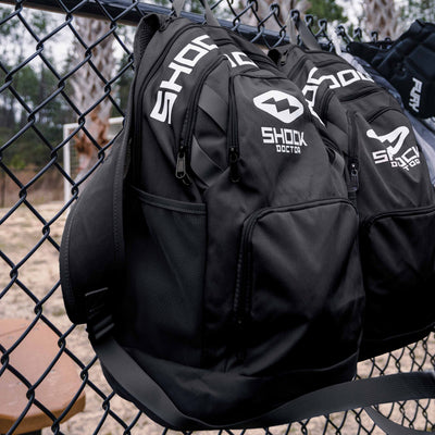 Shock Doctor Premium Backpack - Lifestyle Image 2 - 2 Backpacks Hanging From Chain Link Fence