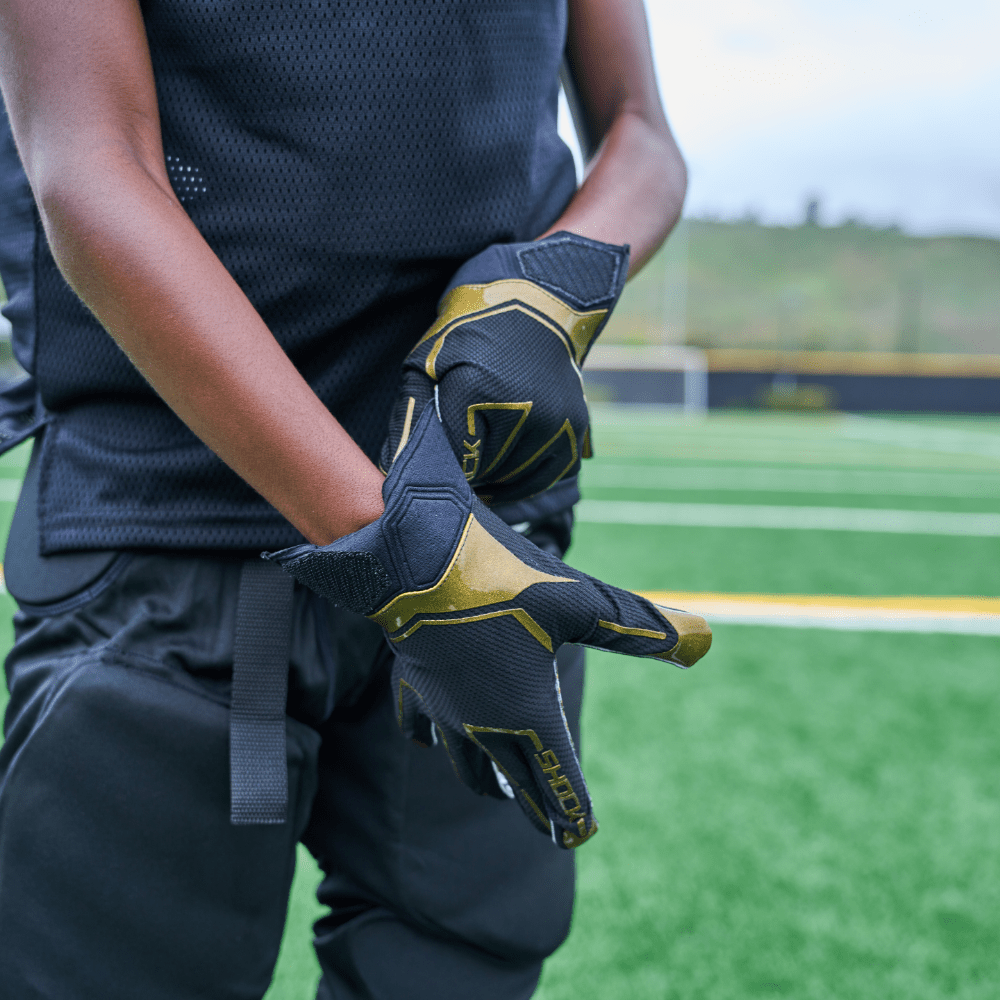 Shock Doctor Black/Gold King Showtime Football Receiver Gloves - Lifestyle Shot of Youth Football Player Pulling Glove Over Right Hand
