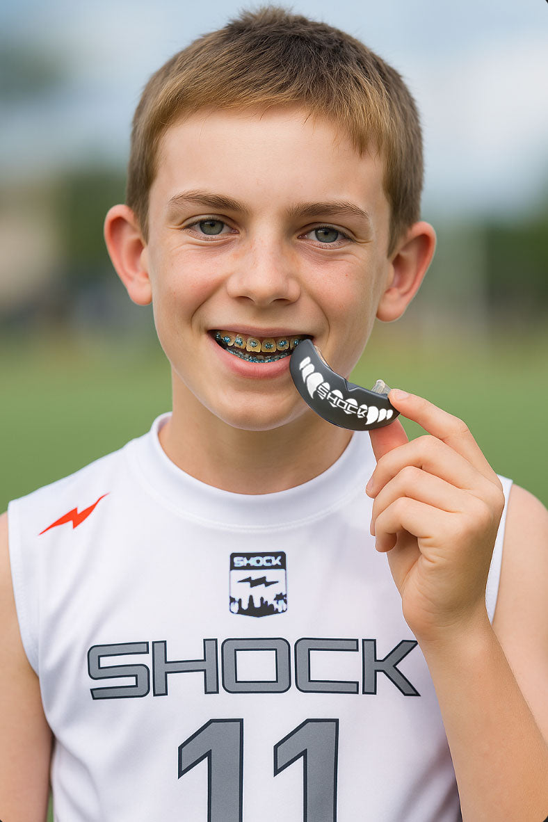 Young boy holding a shock doctor mouthguard with a blurred outdoor background