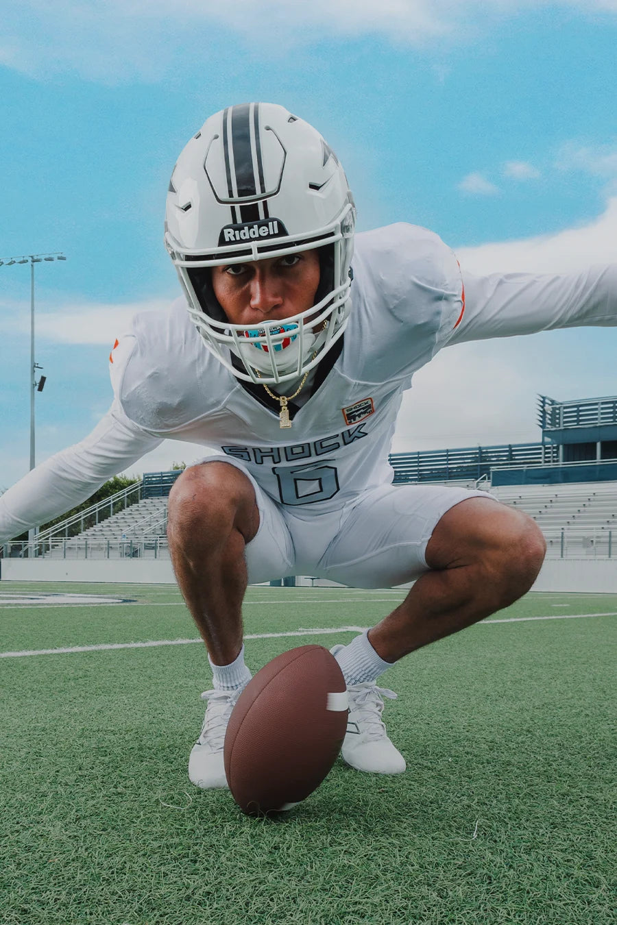Football player in a white uniform with a helmet, holding a football on a field.