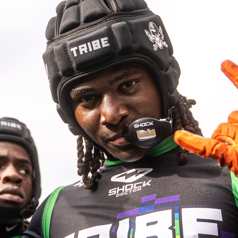 Football player wearing a black Shock Doctor Max AirFlow Lip Guard and padded headgear, posing in Tribe team uniform.
