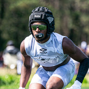 Football player in white camo uniform wearing a black Shock Doctor Max AirFlow Lip Guard, padded headgear, and sunglasses in game stance