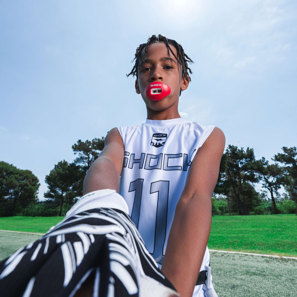 Youth football player in white Shock Doctor uniform wearing a red Shock Doctor Max AirFlow Lip Guard while standing on the field.