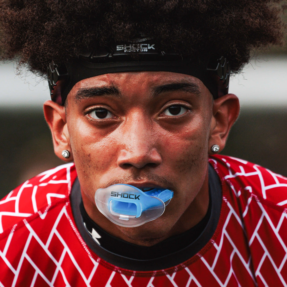 Football player in red patterned uniform wearing a translucent blue Shock Doctor Max AirFlow Lip Guard during game play