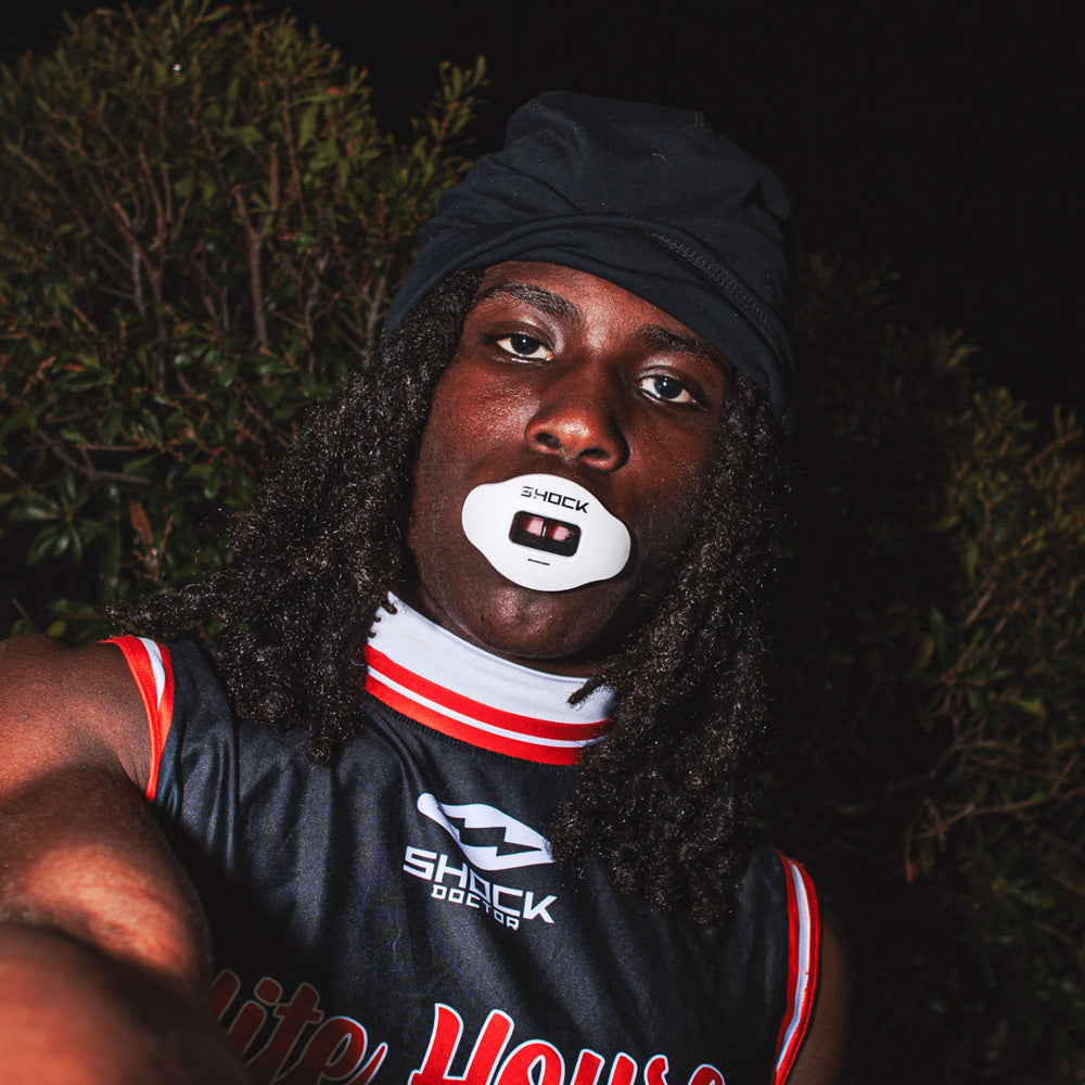 Football player in black and red uniform wearing a white Shock Doctor Max AirFlow Lip Guard at night.