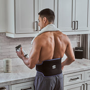 Man in a kitchen holding a shaker bottle, wearing the Shock Doctor Flex Ice Therapy Back Compression Wrap after a workout