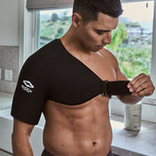 Man in a kitchen adjusting the chest strap on the black Shock Doctor Flex Ice Therapy Shoulder Compression Wrap