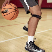 Basketball player dribbling mid-game wearing the Shock Doctor Jumper Knee/Patella Support Strap on their lower leg, paired with a basketball and sneakers