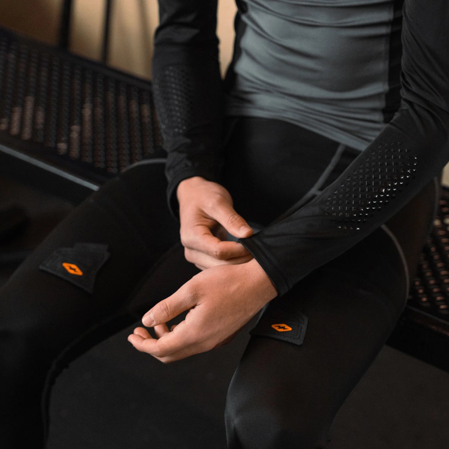 hockey player wearing black hockey pants with orange shock logo accents sitting on a bench