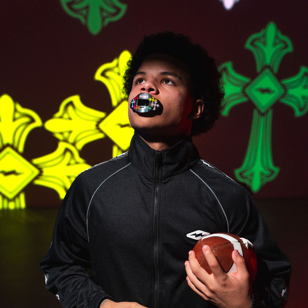 Person holding a football with colorful mouthguard against a dark background with green and yellow designs.