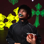 Person holding a football with colorful mouthguard against a dark background with green and yellow designs.