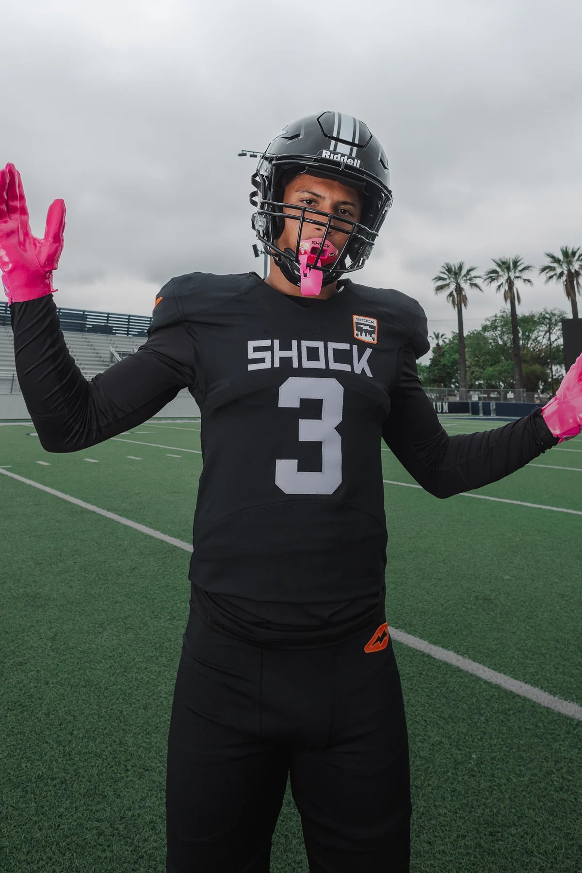 Person in a football uniform with pink gloves and mouthguard on a football field.