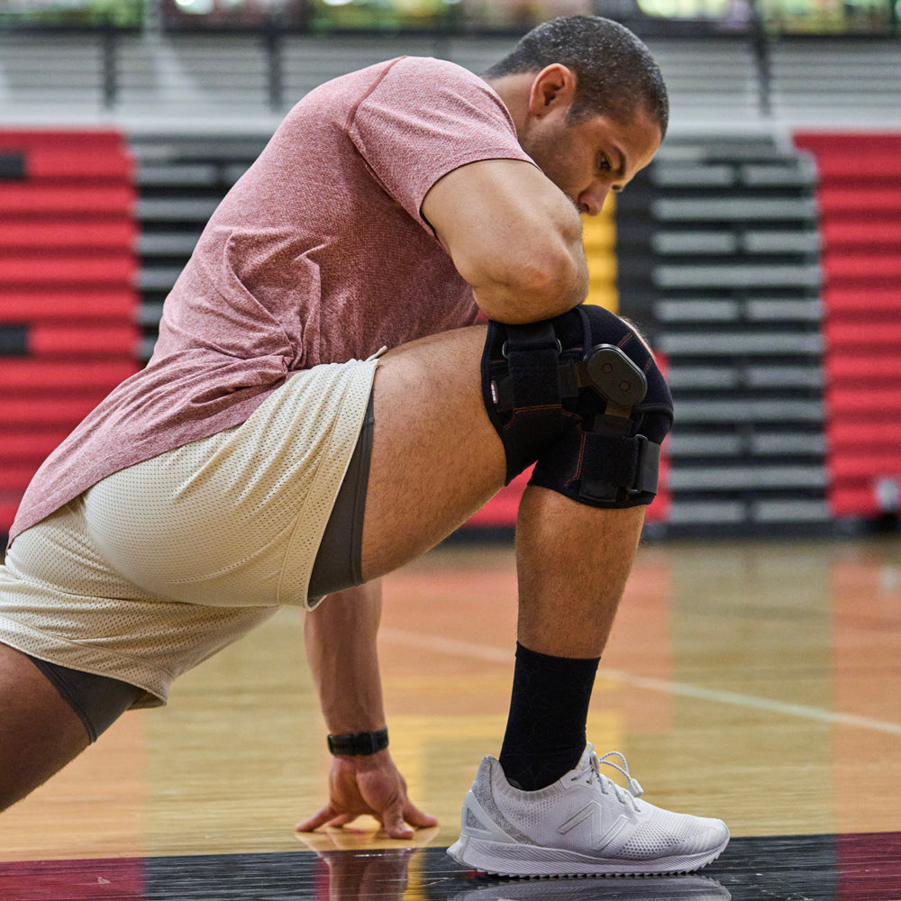 Athlete Wearing Shock Doctor Knee Brace with Dual Wrap & Heavy-Duty Hinges While Stretching