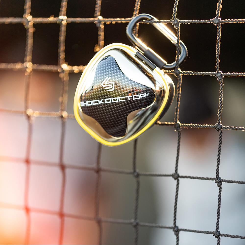 Lifestyle Image of Chrome Gold Mouthguard Case Hanging On Fence with Carabiner